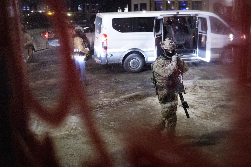 Several federal agents and their van are seen through a window at night.