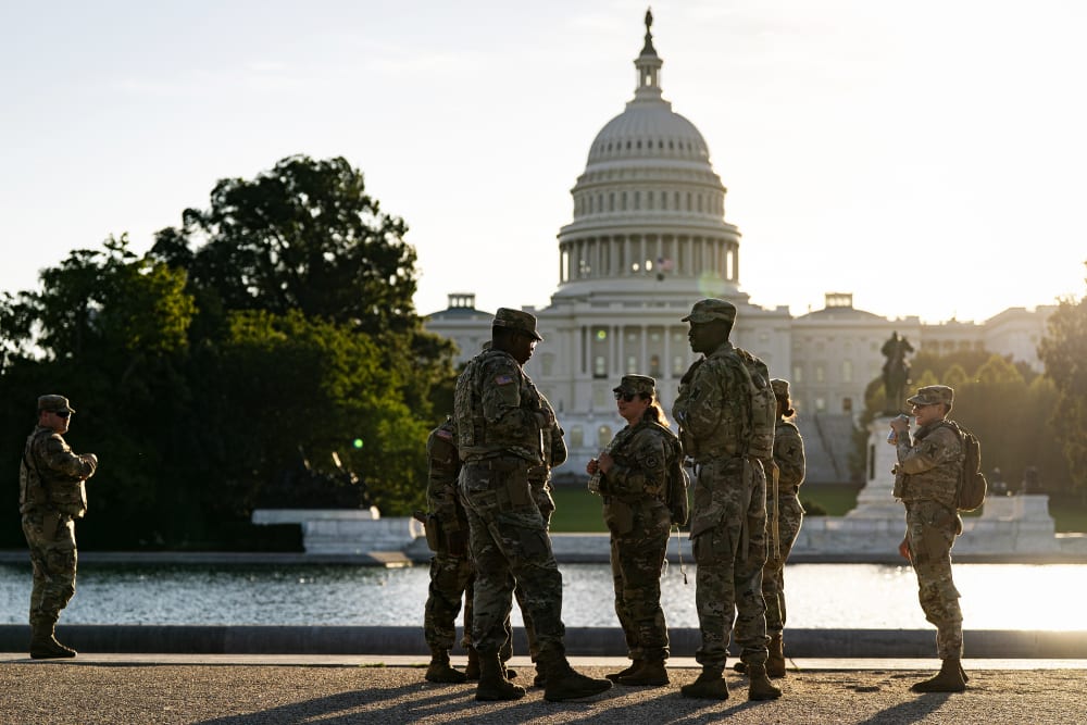 Several National Guard members stand by a pond across from the Capitol at sunset.