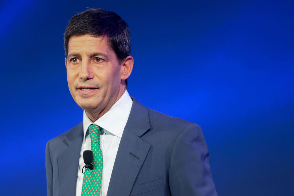 Kevin Warsh seen at the podium with a blue background.