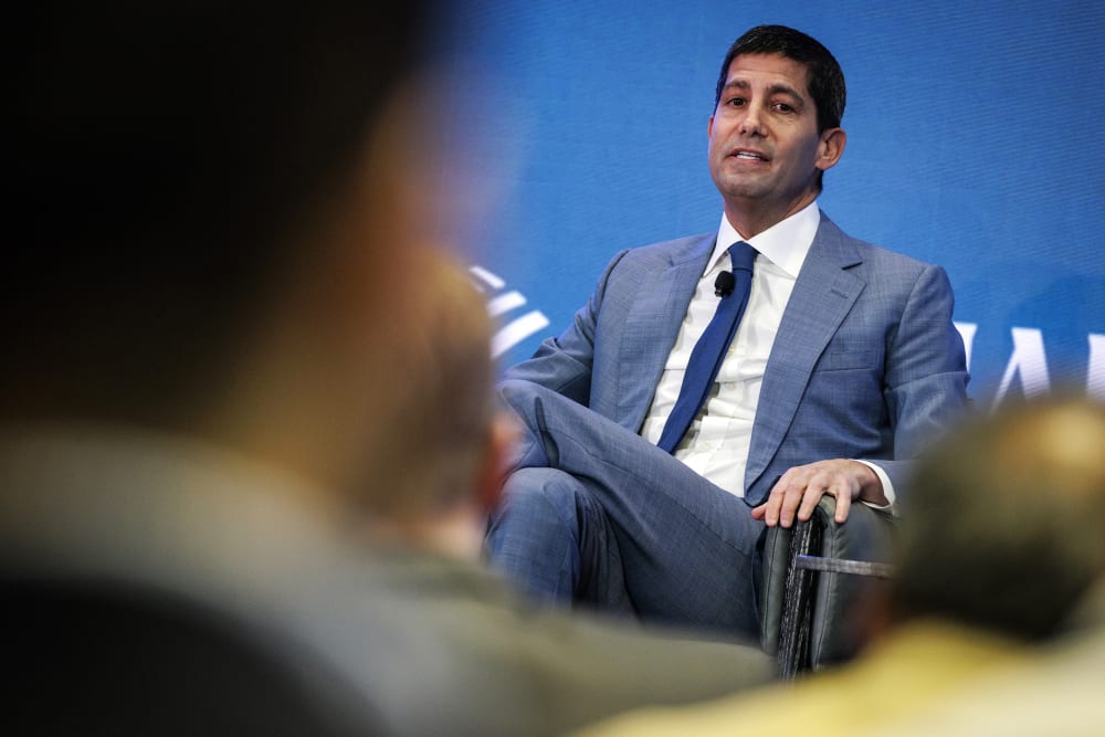 Kevin Warsh sitting on stage seen through heads of the audience.