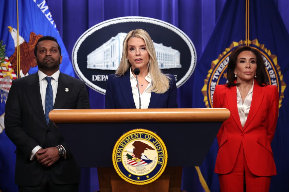Pam Bondi speaks at the podium while Kash Patel and Jeanine Pirro stand behind her.