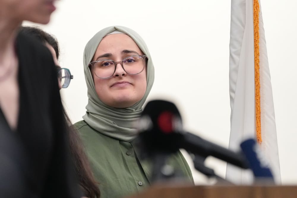 Rumeysa Ozturk looks at the woman speaking at the podium.