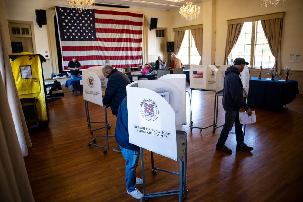 People vote in a polling location with a large American flag in the background.