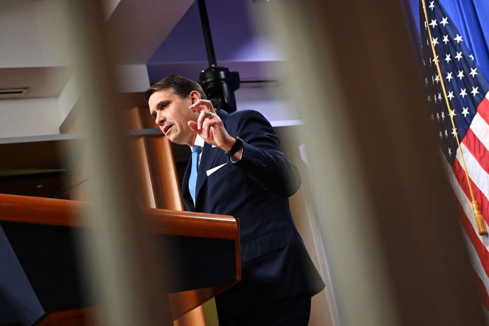Todd Blanche is seen through two white bars as he speaks at a presser.