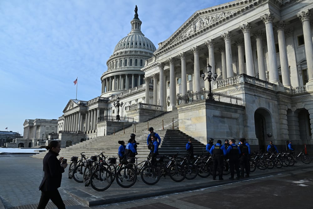 Police officers stand on the side of the capitol building with their bikes.