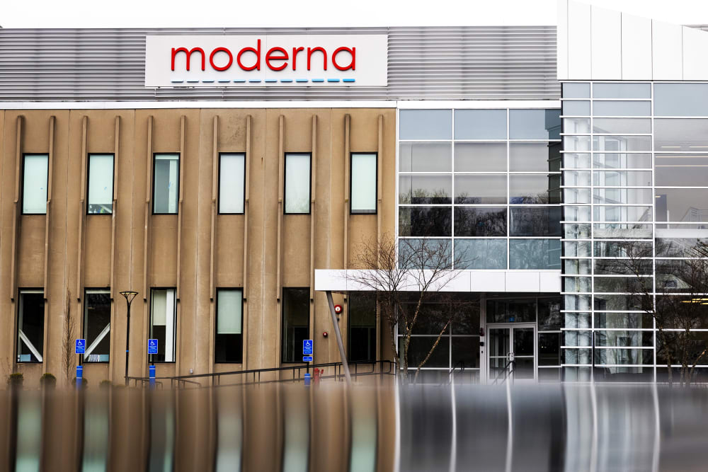 Moderna hq building seen with the red logo. Bottom of the frame shows a reflection of the building potentially on a puddle of water.