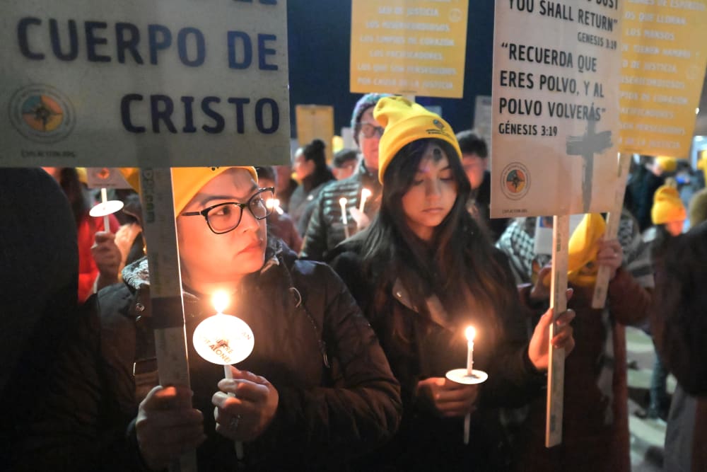 Two women hold candles and signs during a this outdoor Ash Wednesday Mass.