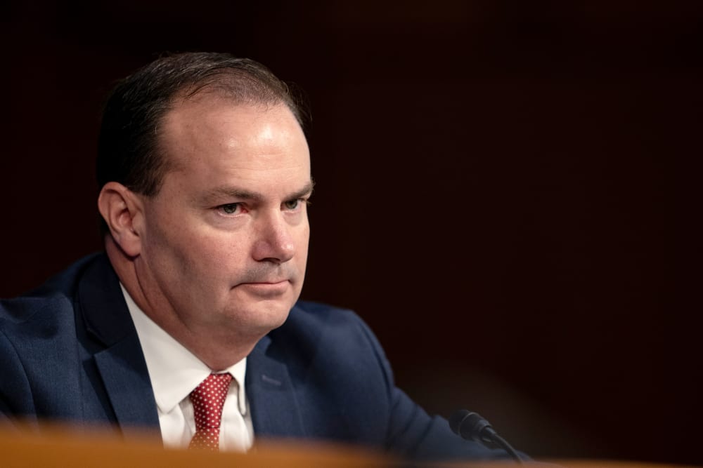 Mike Lee looks on during a hearing. The background is completely black.
