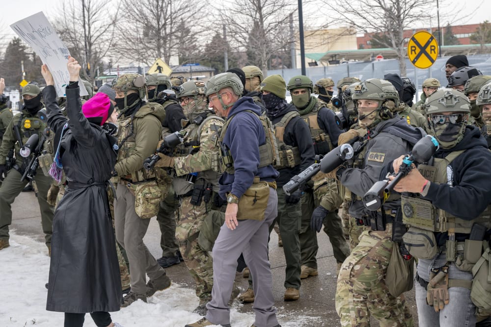 There is one single protestor wearing a a pin k hat in the left side of the frame confronting a large number of federal agents.