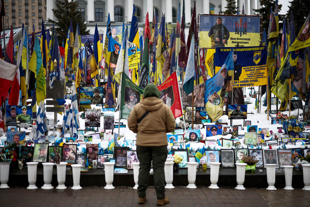 A person stands in front of photos and flags in a memorial.