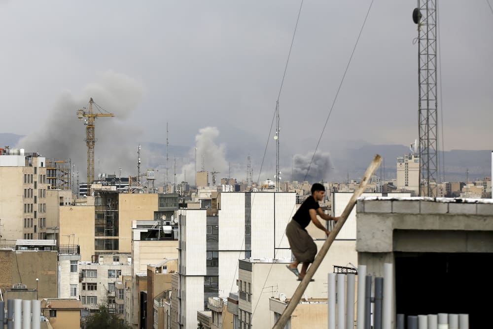 There is a man climbing up stairs while there is smoke rising inthe skyline of Tehran in the background.
