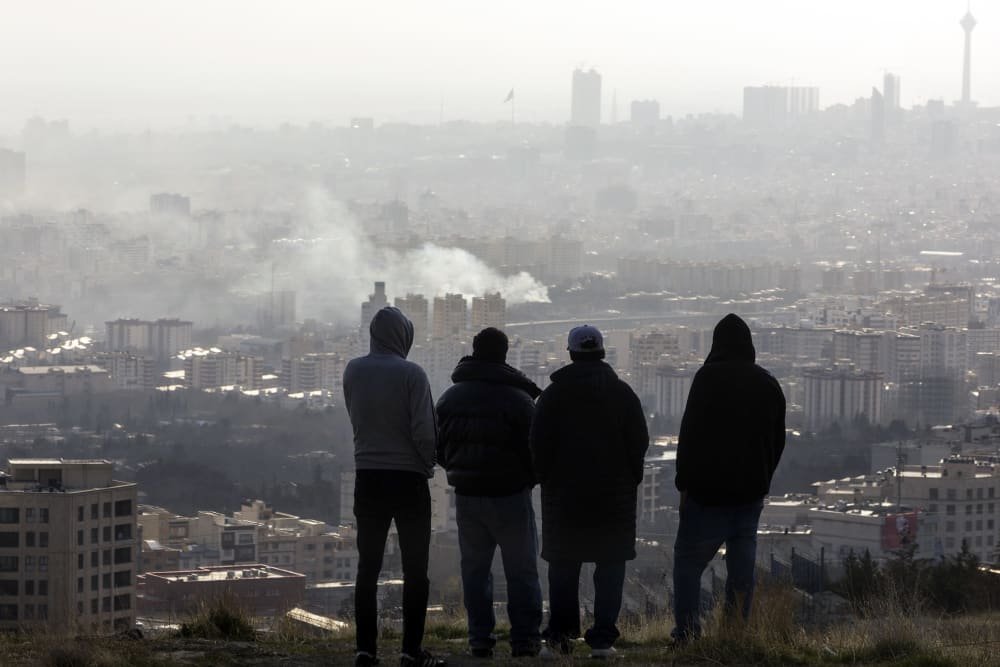 Men watch from a hillside as a plume of smoke rises after an explosion on March 2, 2026 in Tehran.