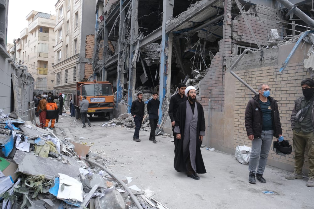 People walk on the street among damaged buildings.