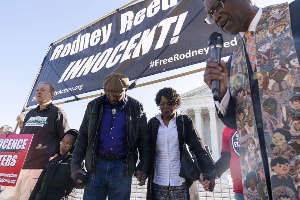 People hold hands looking down as they pray.