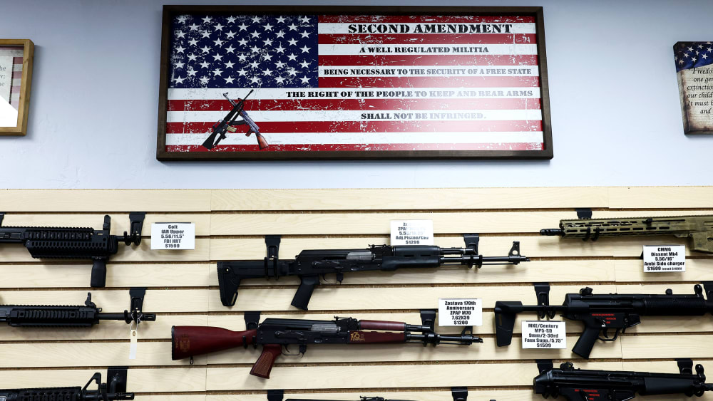 A bunch of weapons are on display below a US flag at a gun store.