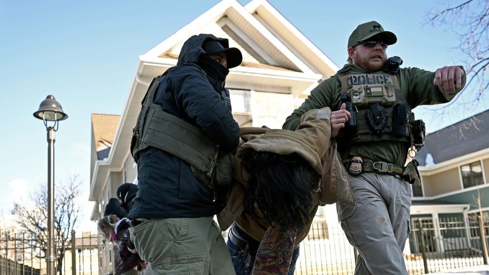 Multiple federal agents drag two people by the arms.