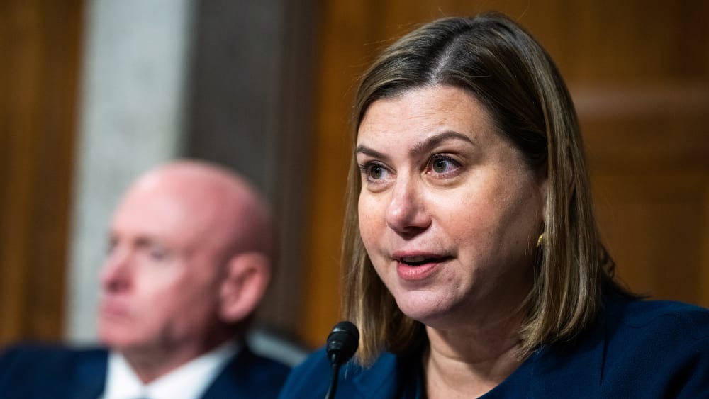 Elissa Slotkin, right, speaks into a microphone. Mark Kelly is out of focus behind her and to her left.