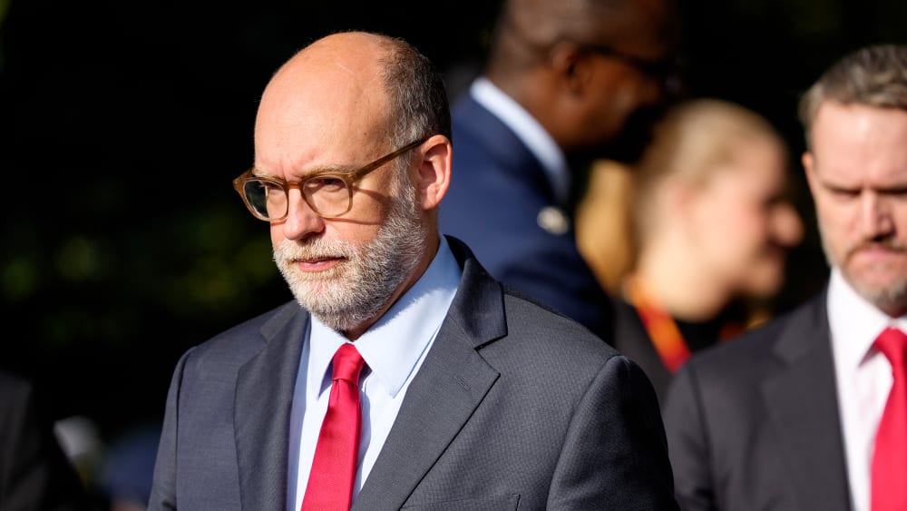 Russell Vought walks in daytime, followed by other people.