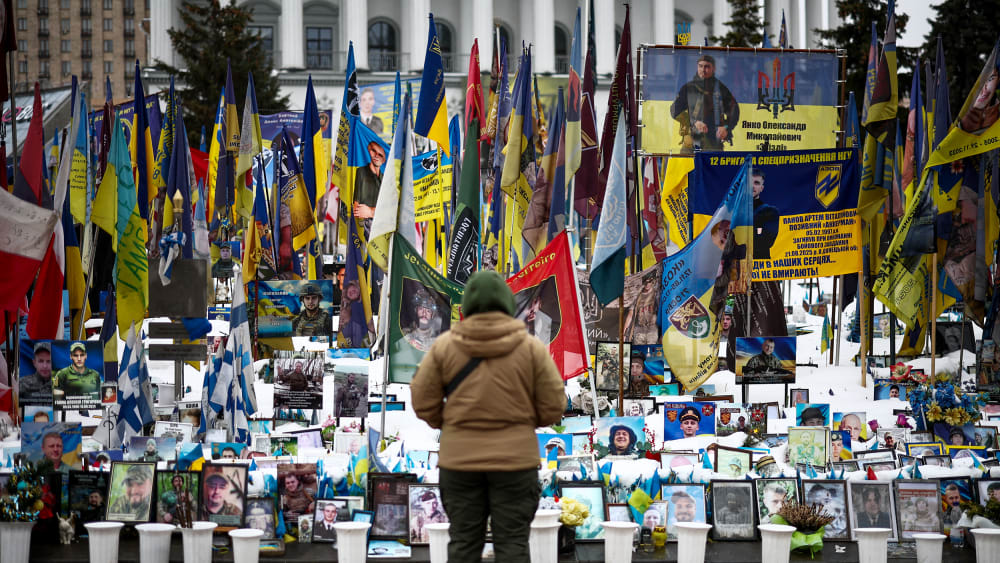 A person stands in front of photos and flags in a memorial.