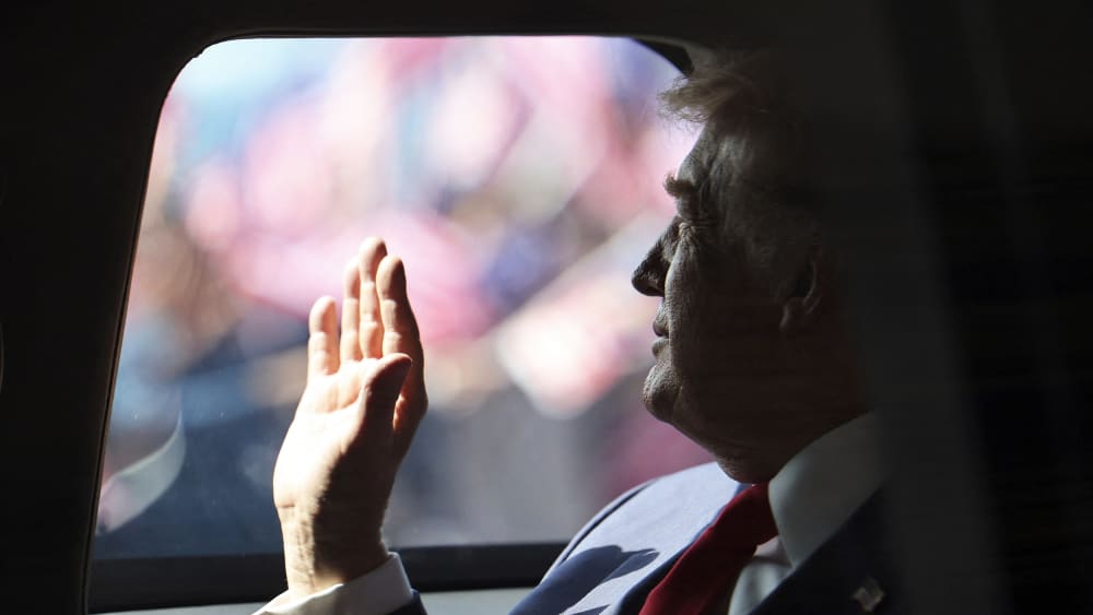 President Donald Trump waves from his official vehicle as he departs from Kuala Lumpur International Airport.