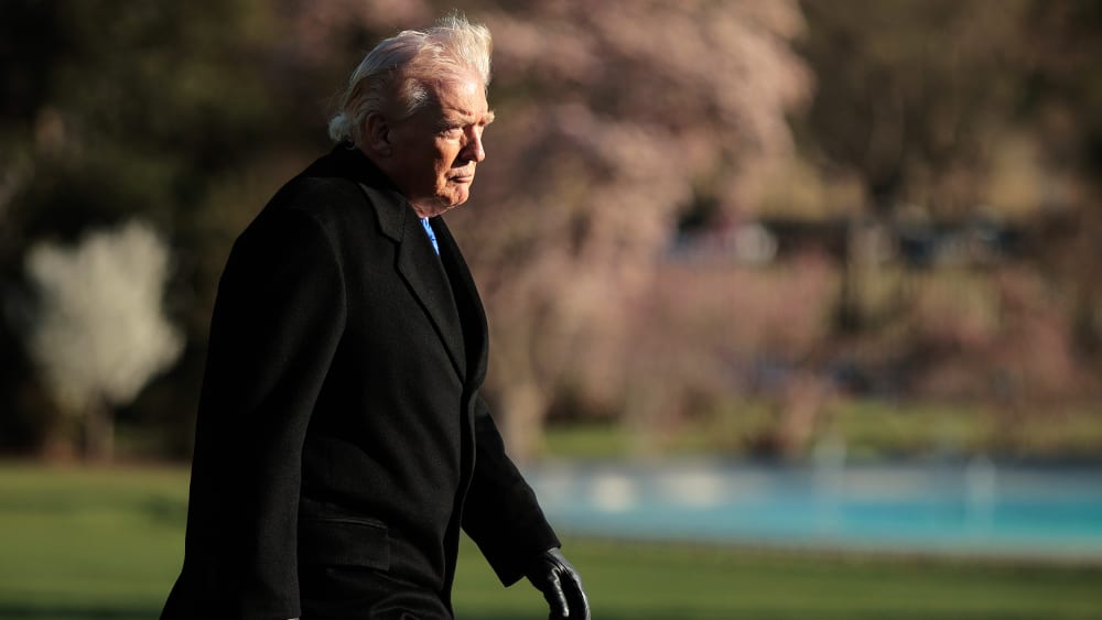 Donald Trump walks at sunset toward the White House building.