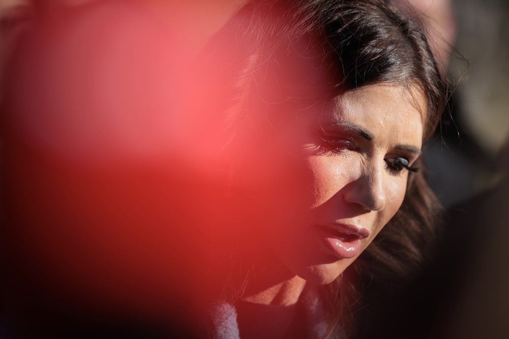Kristi Noem is seen in a very close up shot, an out of focus red spot on the left obscures part of her face.