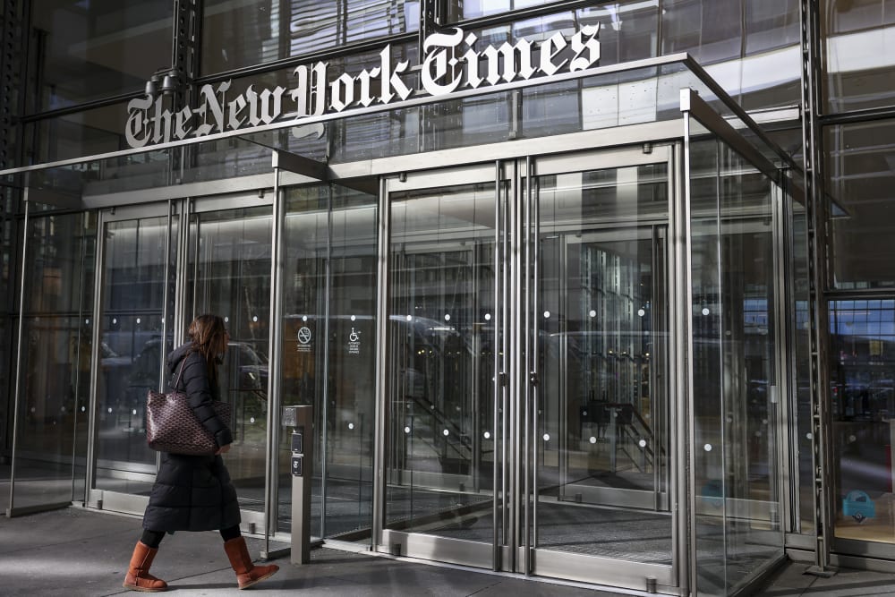 A woman walks into the New York Times building where we can fully see the building sign in the frame.