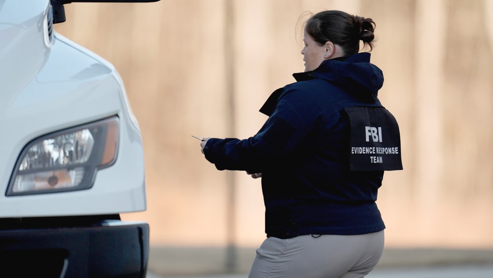 A female FBI officer stands near a white truck. Back of her jacket reads "FBI Evidence Response Team."