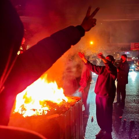 People gather around a fire lit on the streets of Tehran.