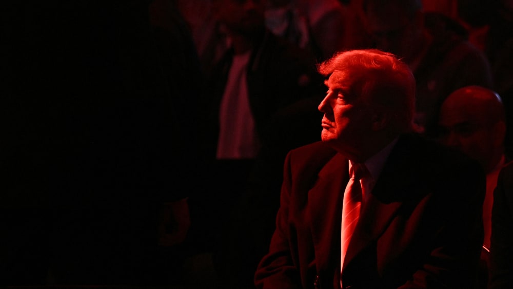 Donald Trump looks into the distance. He and the crowd are basked in red light.