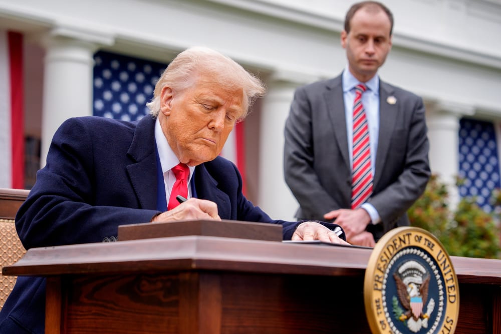 President Trump signs a document at his desk about imposing tariffs.