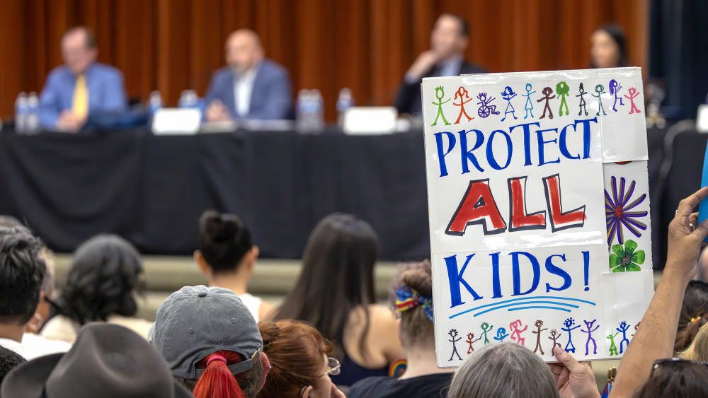 An attendee holds a sign that reads "Protet All Kids" seen from behind.