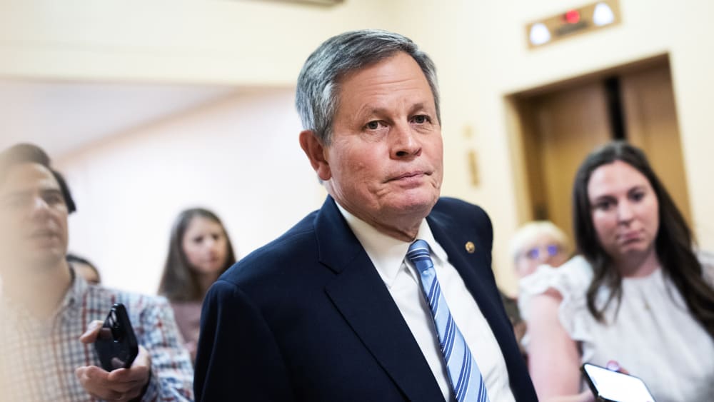 Steve Daniels walks in the direction of the camera as journalists follow him asking questions.