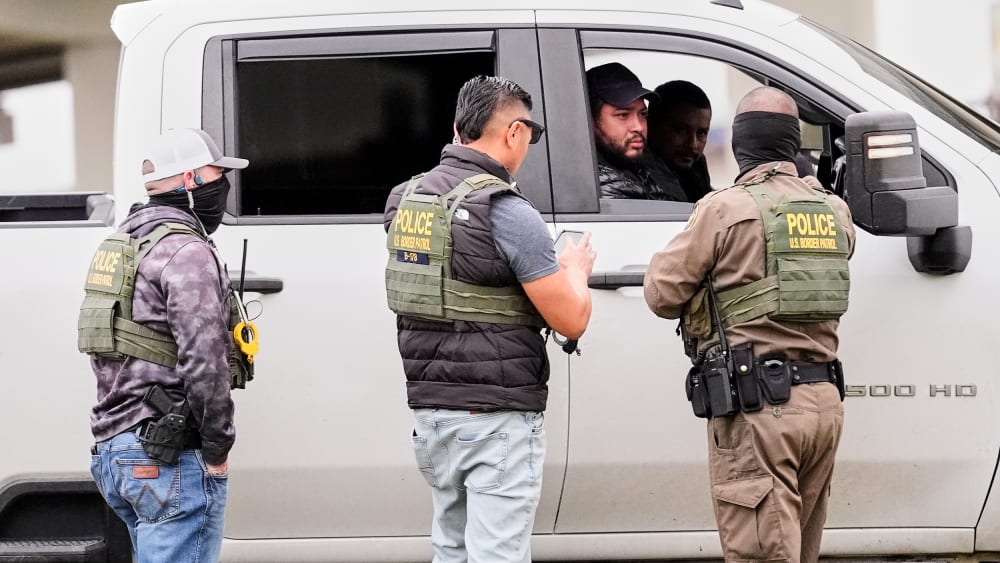 Three federal agents talk to two men in a white truck.