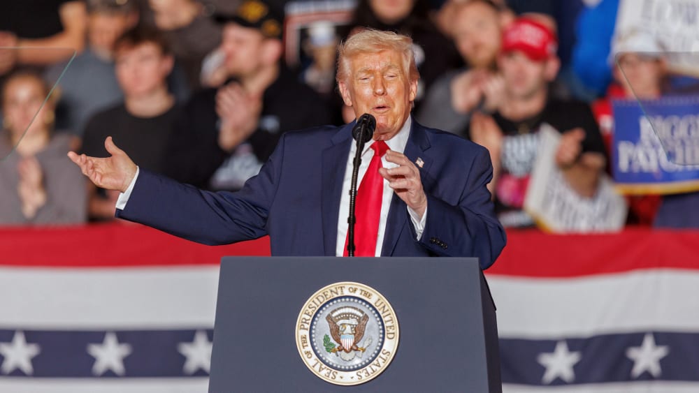 Donald Trump gestures behind a podium in front of an audience.