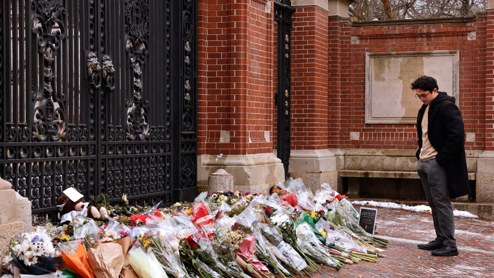 A student stands at the Van Wickle Gates of Brown University after laying down flowers.