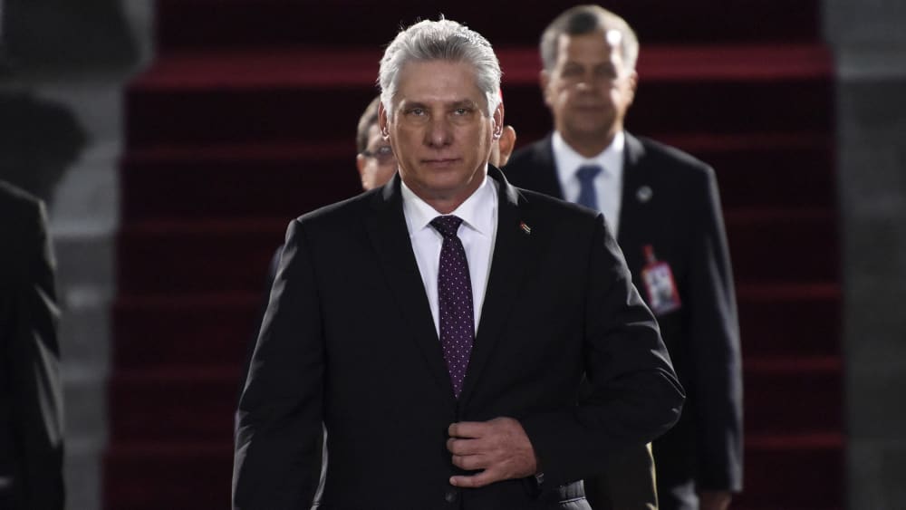 Miguel Díaz-Canel walks toward the camera with his hand on his suit jacket's button.