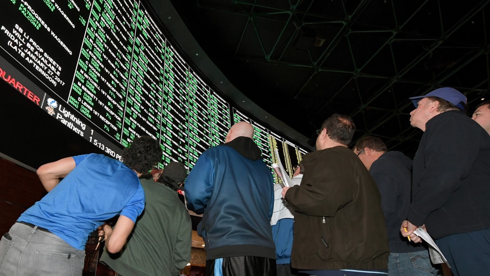 People look up toward a betting odds video board.