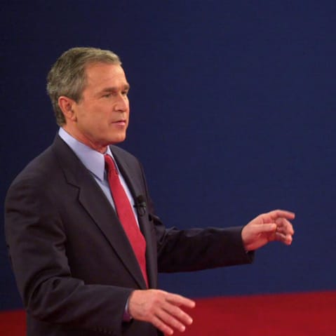 George Bush speaks to Al Gore while Gore reacts by opening both arms.