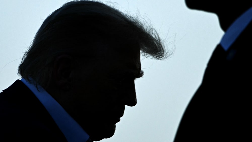 Trump's profile is seen as he walks up to the place. A security person stands on the right side.
