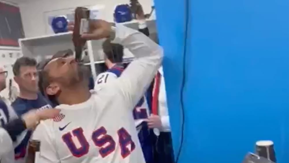 Kash Patel chugs a bottle of beer in front of hockey players.