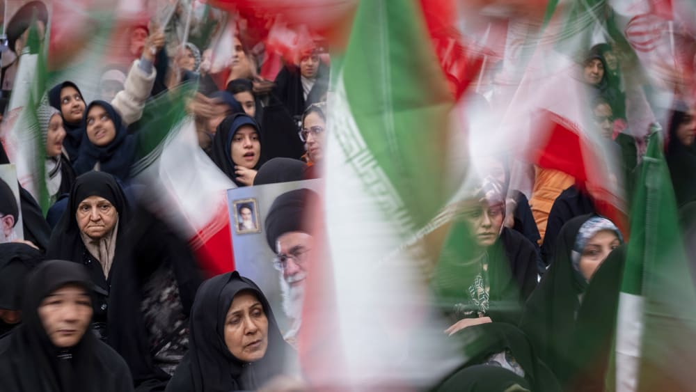Women wave Iranian flags, which are blurred in motion.