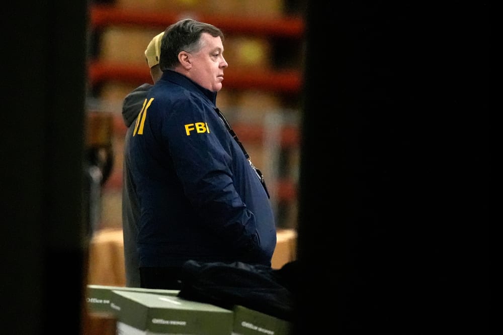 An FBI agent is seen standing near green boxes.