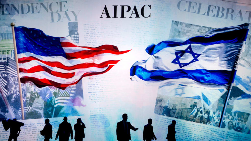 People are silhouetted before a screen that reads "AIPAC" and shows a visual of the American flag and the Israeli flag.