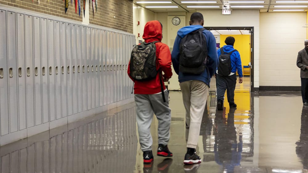 Three students seen from behind as they walk down a high school hallway.