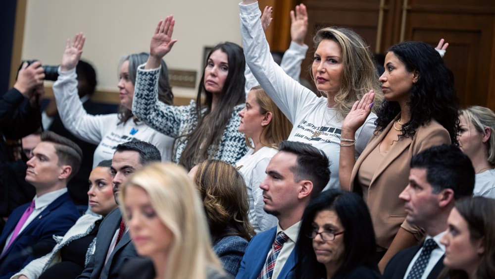 People in focus in the background raise their hands; Pam Bondi out of focus in the foreground looks down.