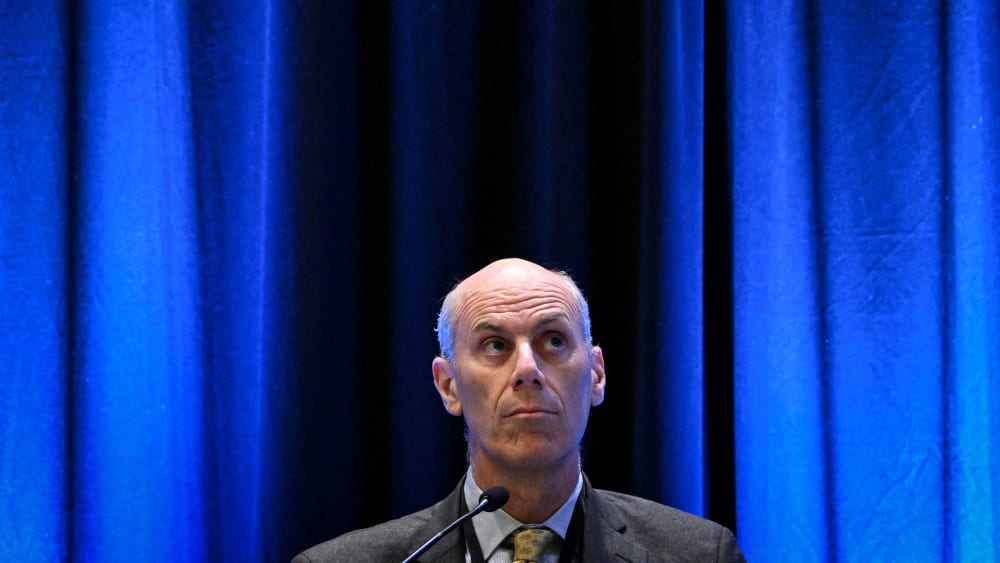 James Boasberg looks up in front of a plain blue background.