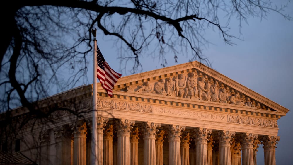 The U.S. flag flies in front of the Supreme Court building at sunset.