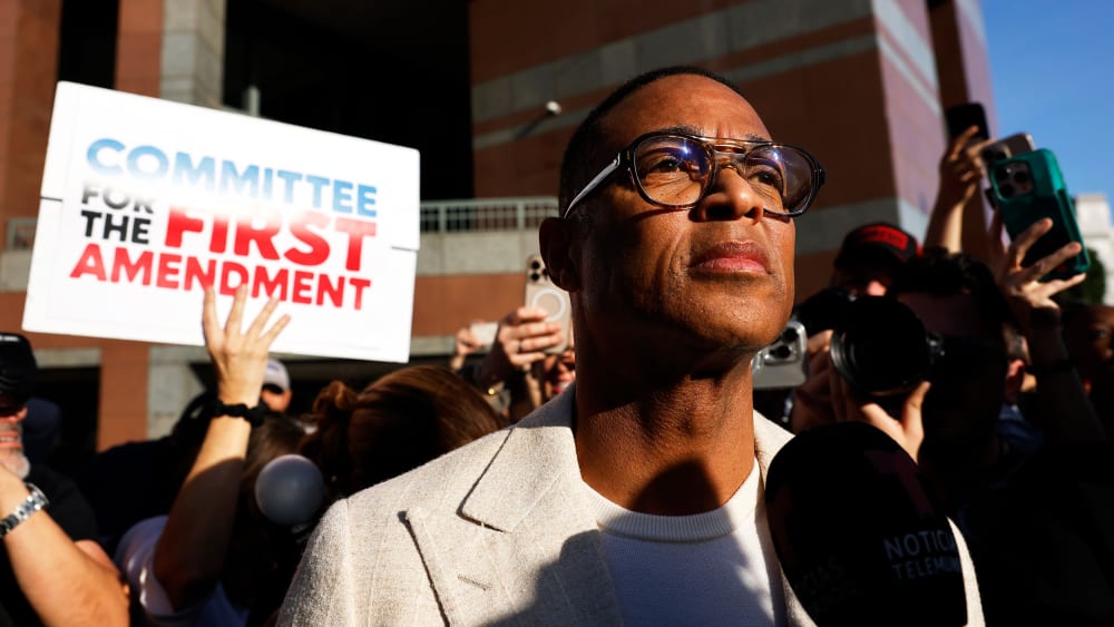 Don Lemon surrounded by people documenting with cameras and cell phones. A person behind him holds a sign that reads "Committee for the First Amendment."