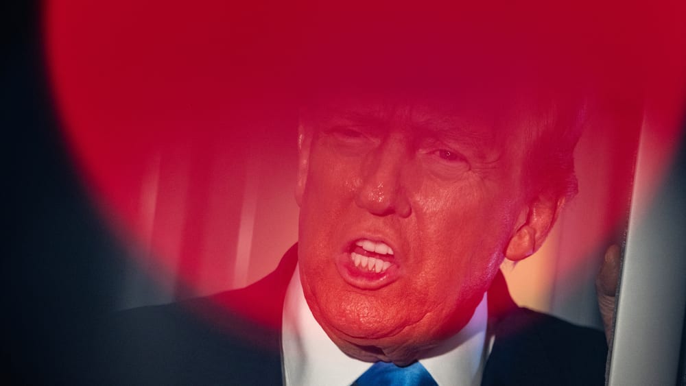 Top part of Donald Trump's face is seen through a round red light.